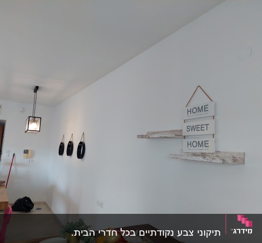 קיר לבן עם שלט "HOME SWEET HOME" ומדפים מעץ